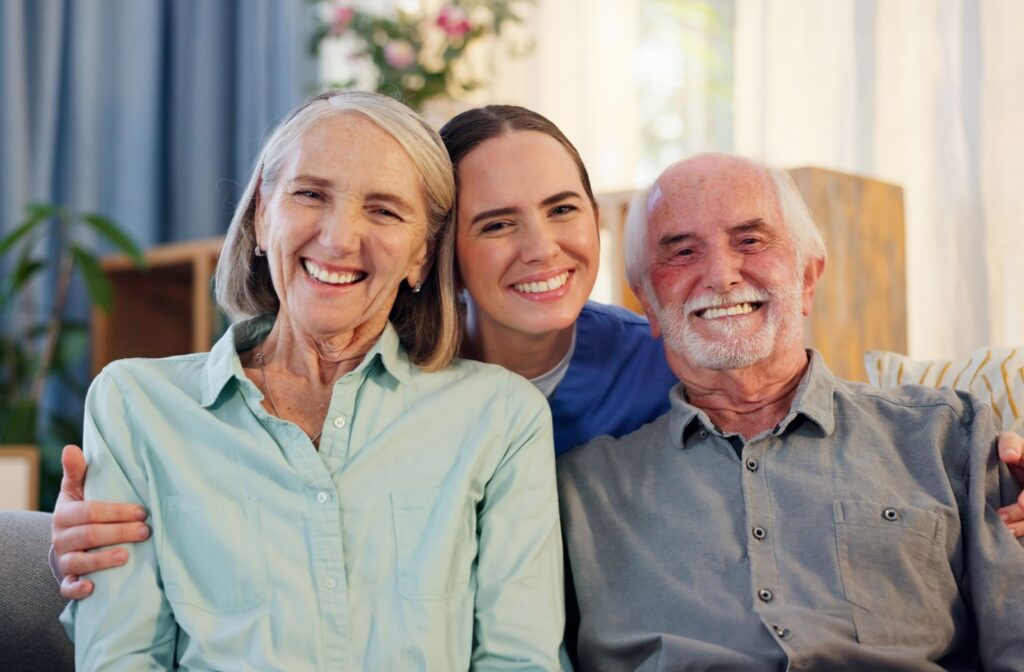 A married couple in senior living and a caregiver all smiling with arms around each other.