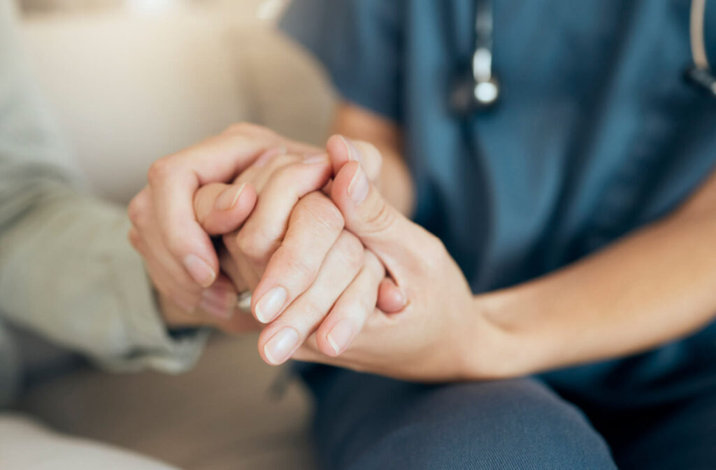 A caregiver holding an older adult's hand to support them in assisted living.